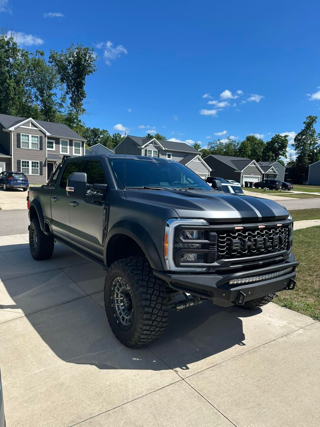 Gray lifted Ford pickup truck with black trim, parked on a driveway.