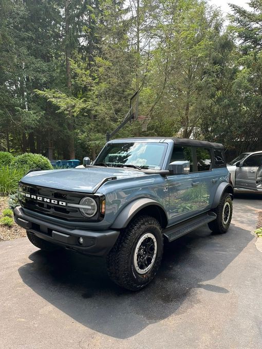 Blue Ford Bronco SUV parked on a paved driveway with trees in the background.