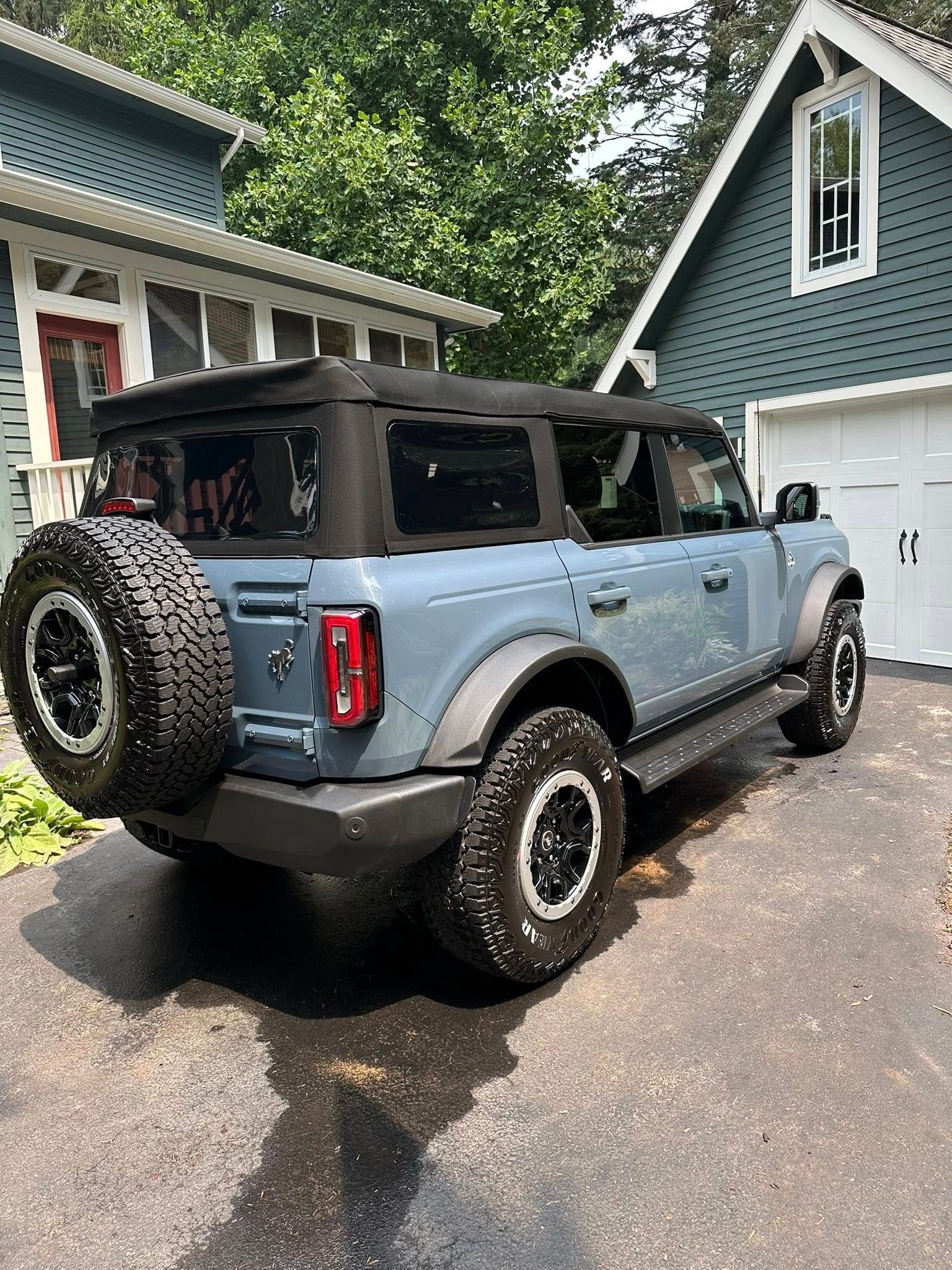 Blue Ford Bronco parked on a driveway, soft top, near a house with a garage.