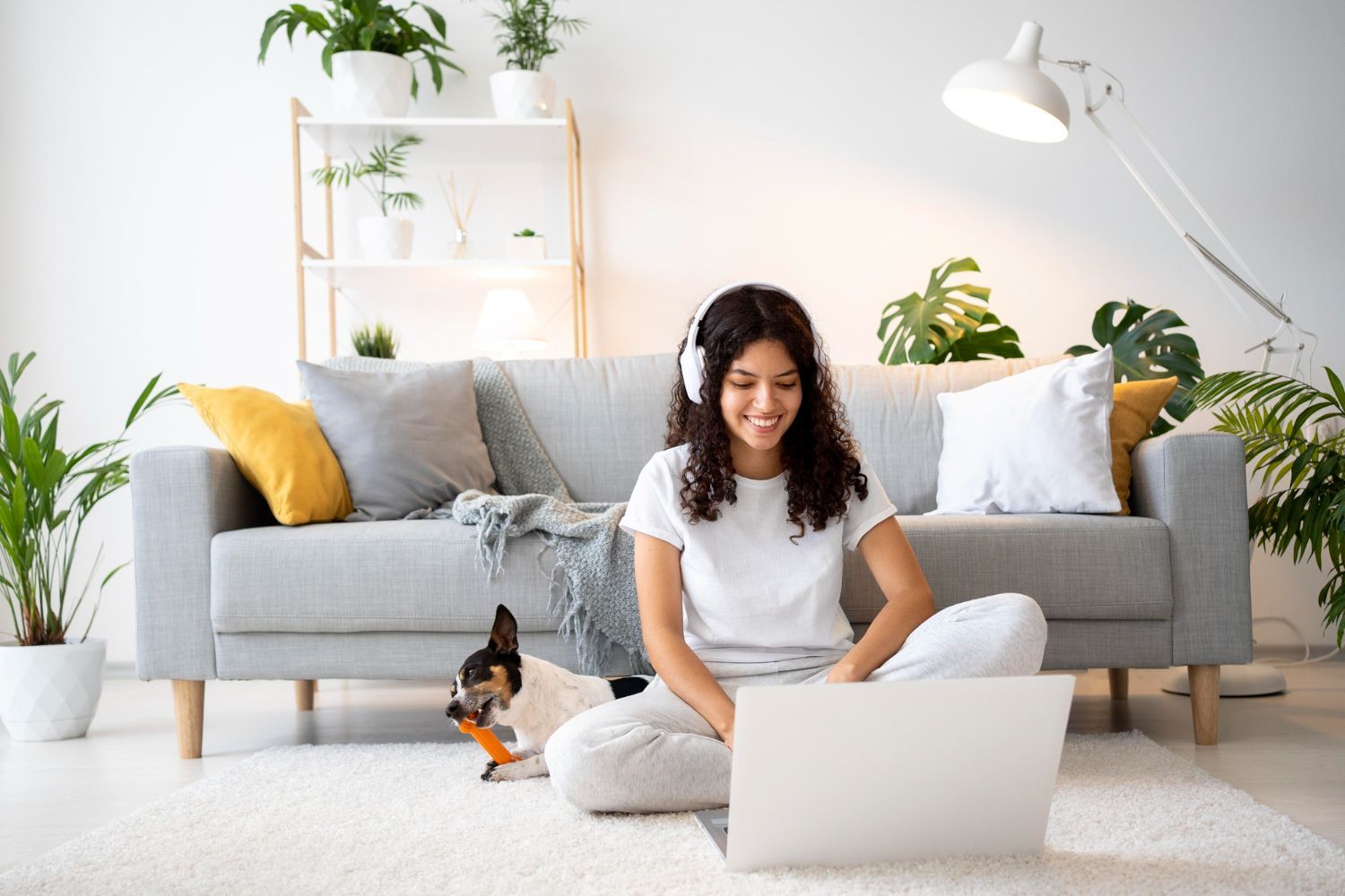 A woman is sitting on the floor in front of a couch using a laptop computer.