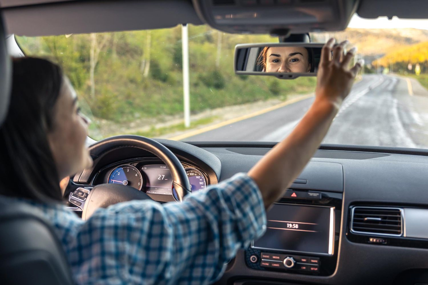 A woman is adjusting the rear view mirror of her car.
