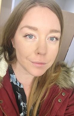 A woman wearing a red jacket with a fur hood is taking a selfie.