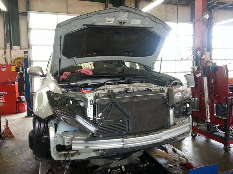 A silver car with its hood open and front bumper removed, positioned inside an auto repair shop. | Auto Service Depot