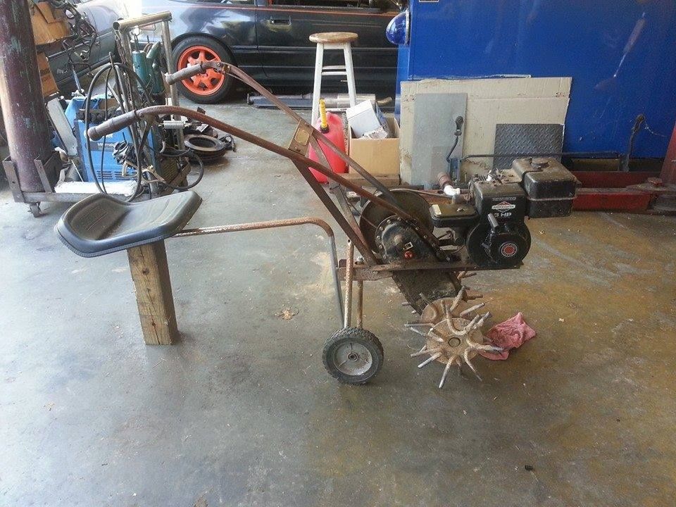 A DIY motorized tiller with a seat attachment and small support wheel in a workshop setting. | Auto Service Depot