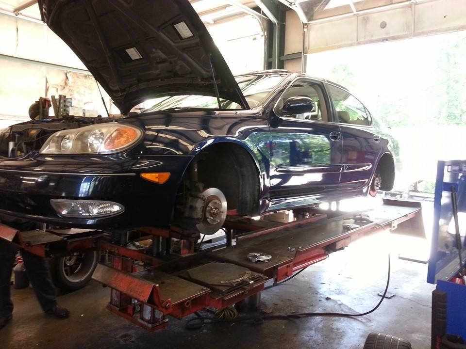 A dark blue car with its front wheel removed is raised on a hydraulic lift inside an auto repair shop. | Auto Service Depot
