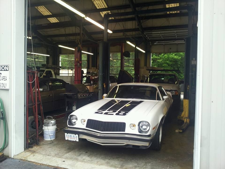 A white Chevrolet Camaro Z28 with black racing stripes parked inside an automotive repair shop garage. | Auto Service Depot