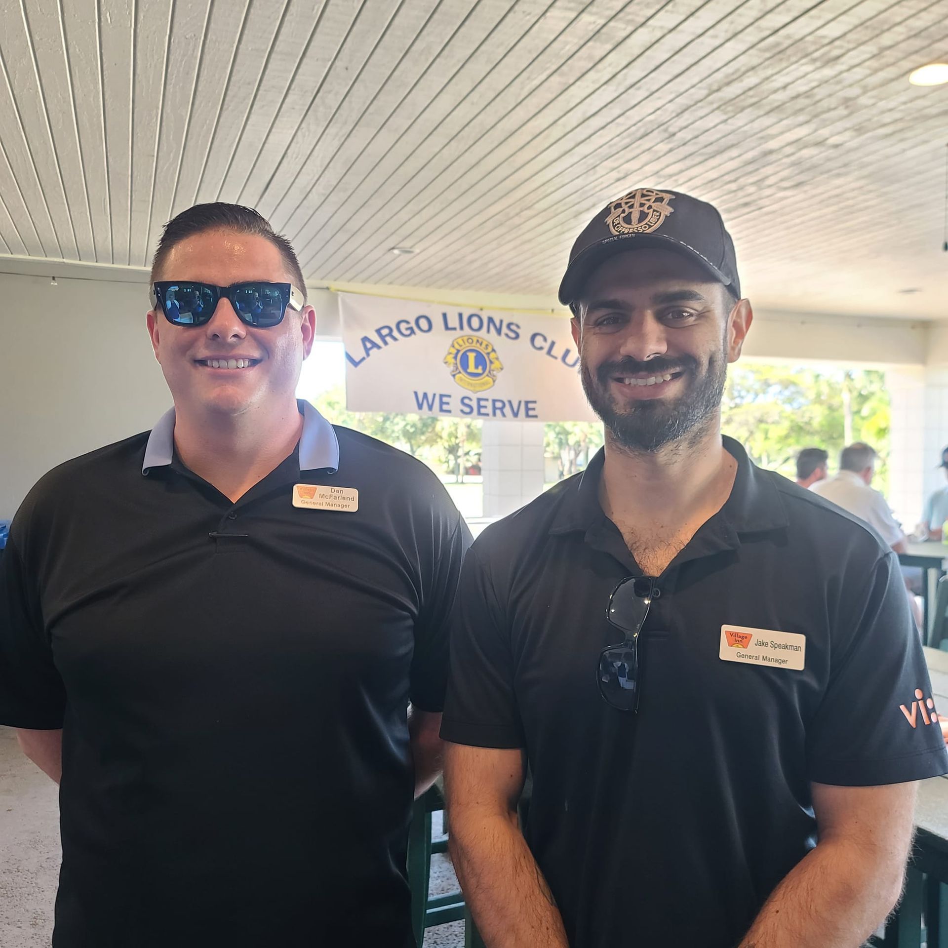 Two men are posing for a picture in front of a sign that says largo lions club we serve
