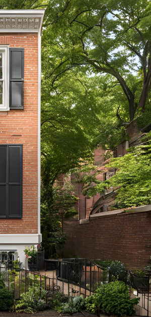 A brick house with black shutters is surrounded by trees and bushes.
