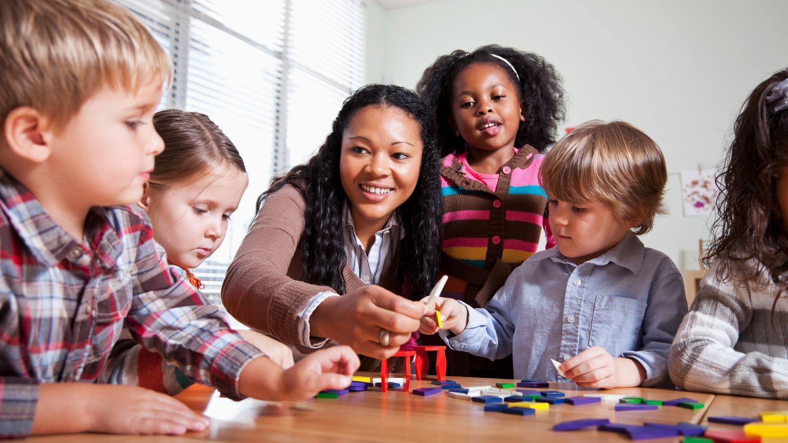 Teacher and children building with colorful blocks at a table.