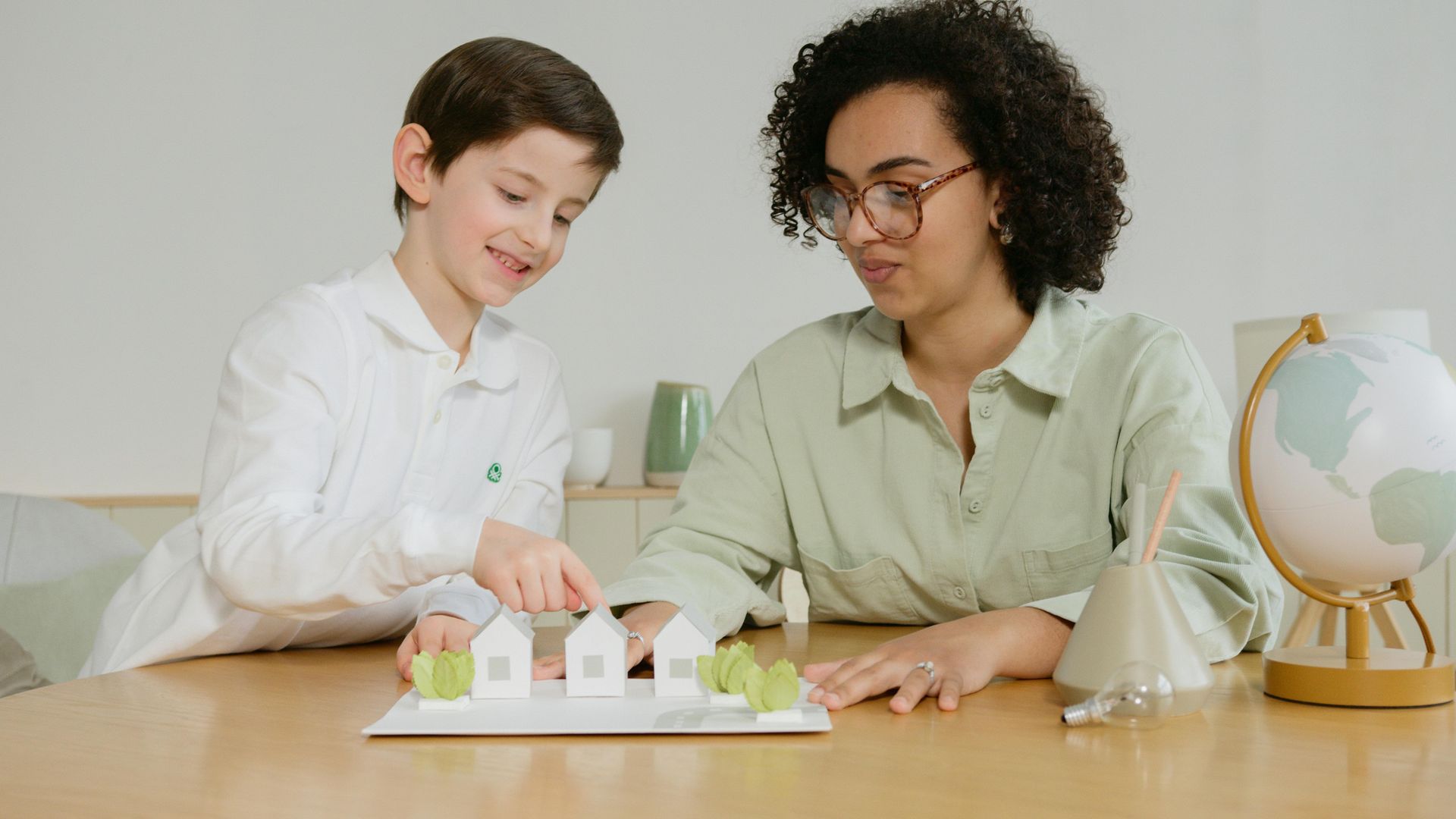 Boy and woman examining a model of houses, smiling, at a table with a globe.