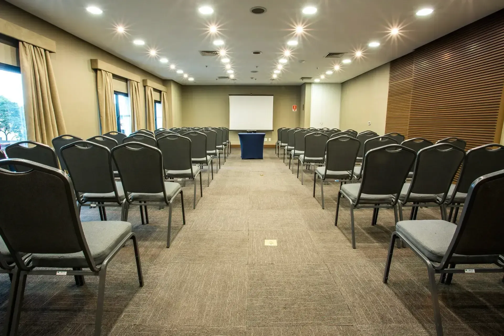 uma grande sala de conferências com fileiras de cadeiras e uma tela de projeção.