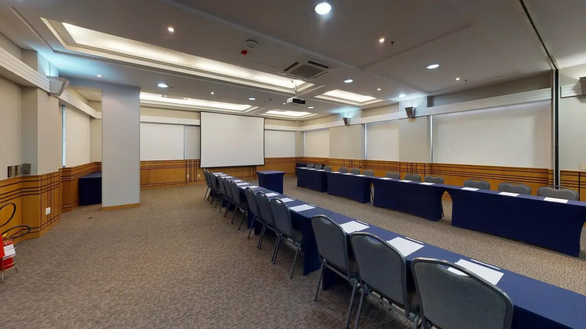 uma grande sala de conferências com mesas e cadeiras e uma tela de projeção.