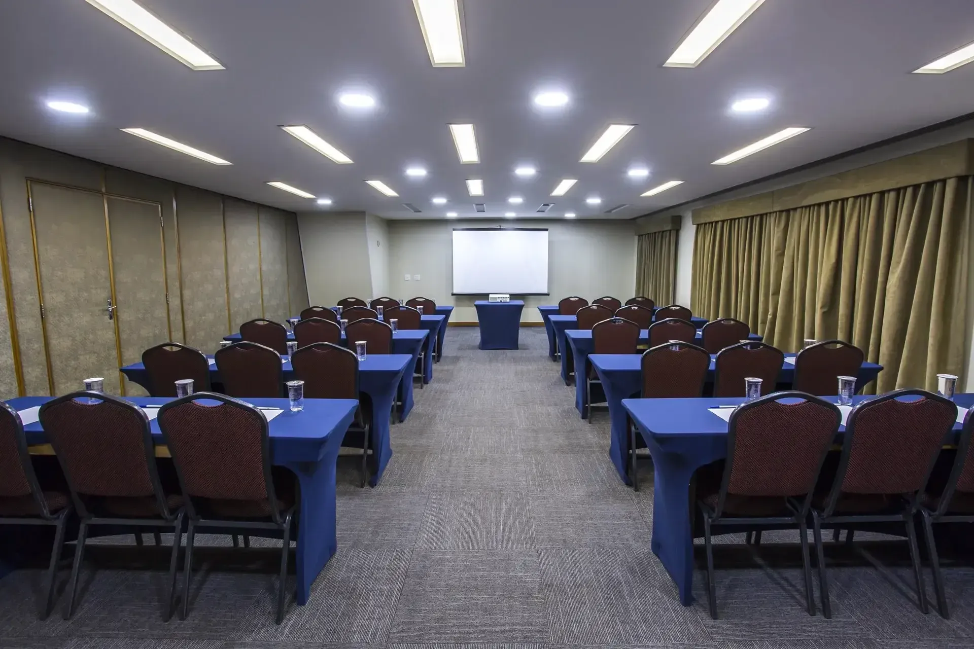 uma sala de conferências com mesas e cadeiras e uma tela de projeção.