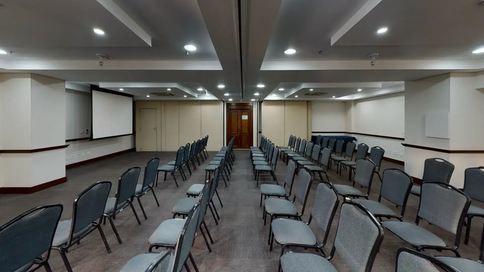 uma grande sala de conferências com fileiras de cadeiras e uma tela de projeção.