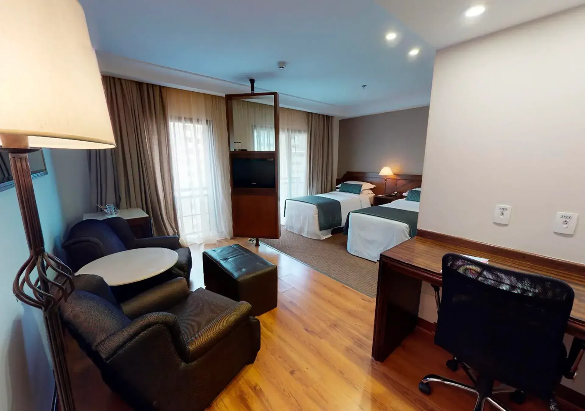 um quarto de hotel com duas camas, uma escrivaninha, uma cadeira e um abajur.