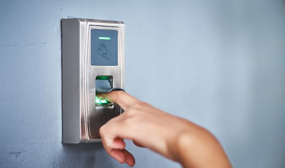 Finger on a fingerprint scanner, mounted on a blue wall. Green light indicates a successful scan.
