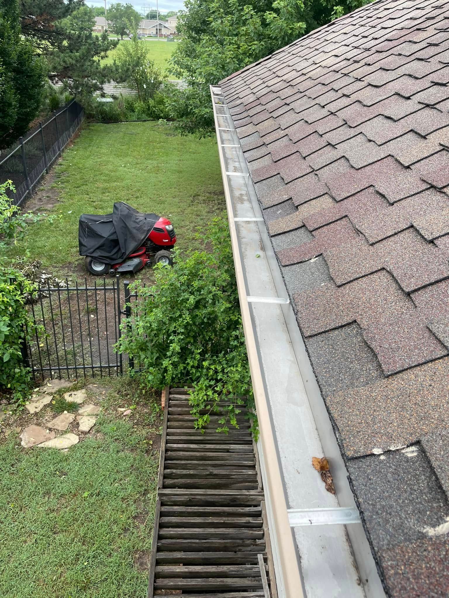 A gutter on the roof of a house with a lawn mower parked in the backyard.