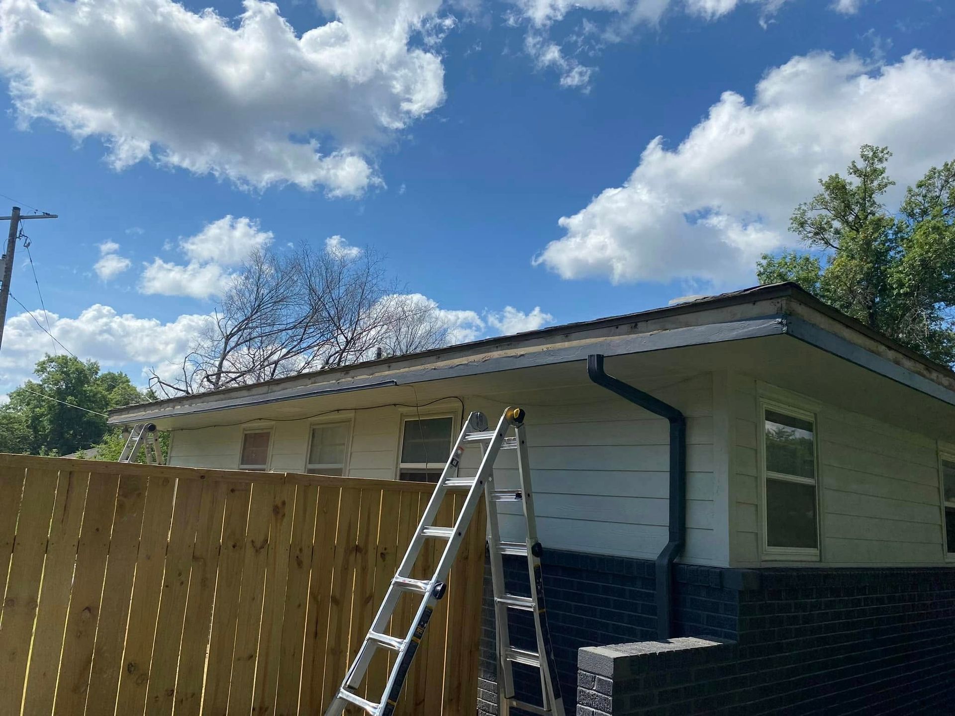 A ladder is sitting on the side of a house next to a wooden fence.