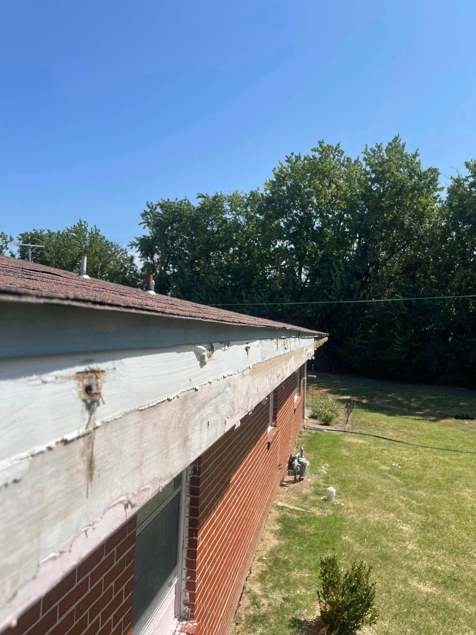 A brick building with a gutter on the side of it and trees in the background.