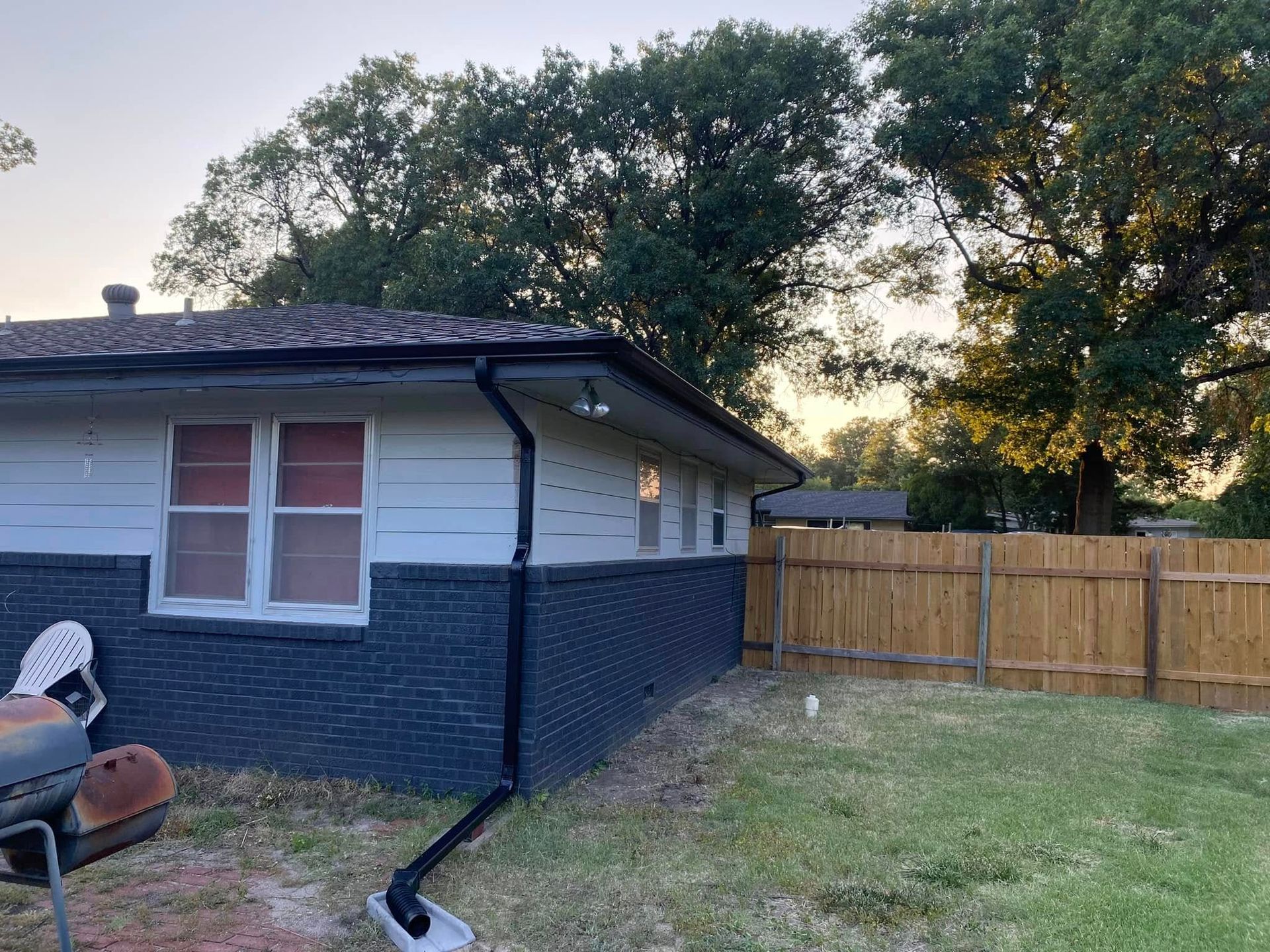 The backyard of a house with a wooden fence and trees in the background.