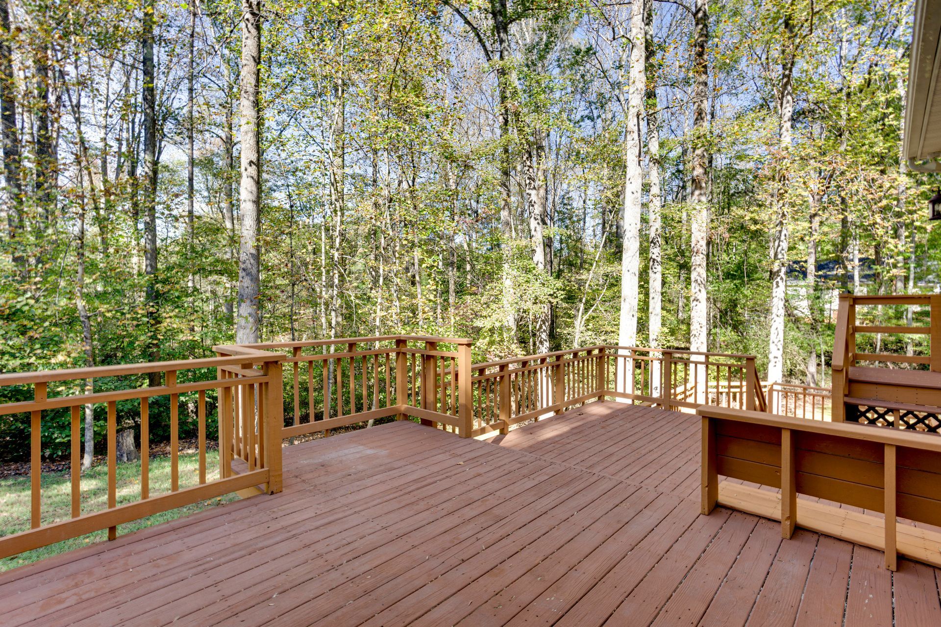 A large wooden deck with a wooden railing is surrounded by trees.
