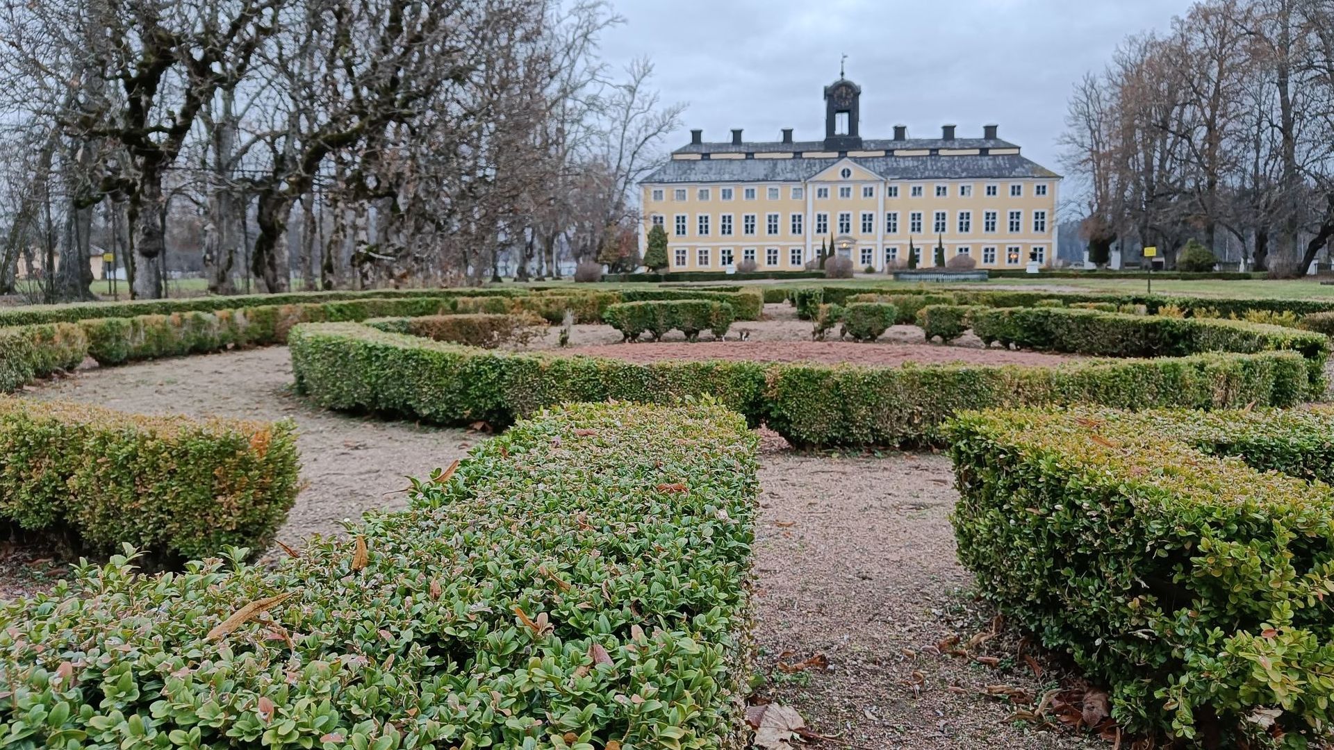 Den franska parken vid Sturefors slott, med låga häckar av buxbom i vackra, symmetriska mönster. I bakgrunden syns det ljusgula slottet.
