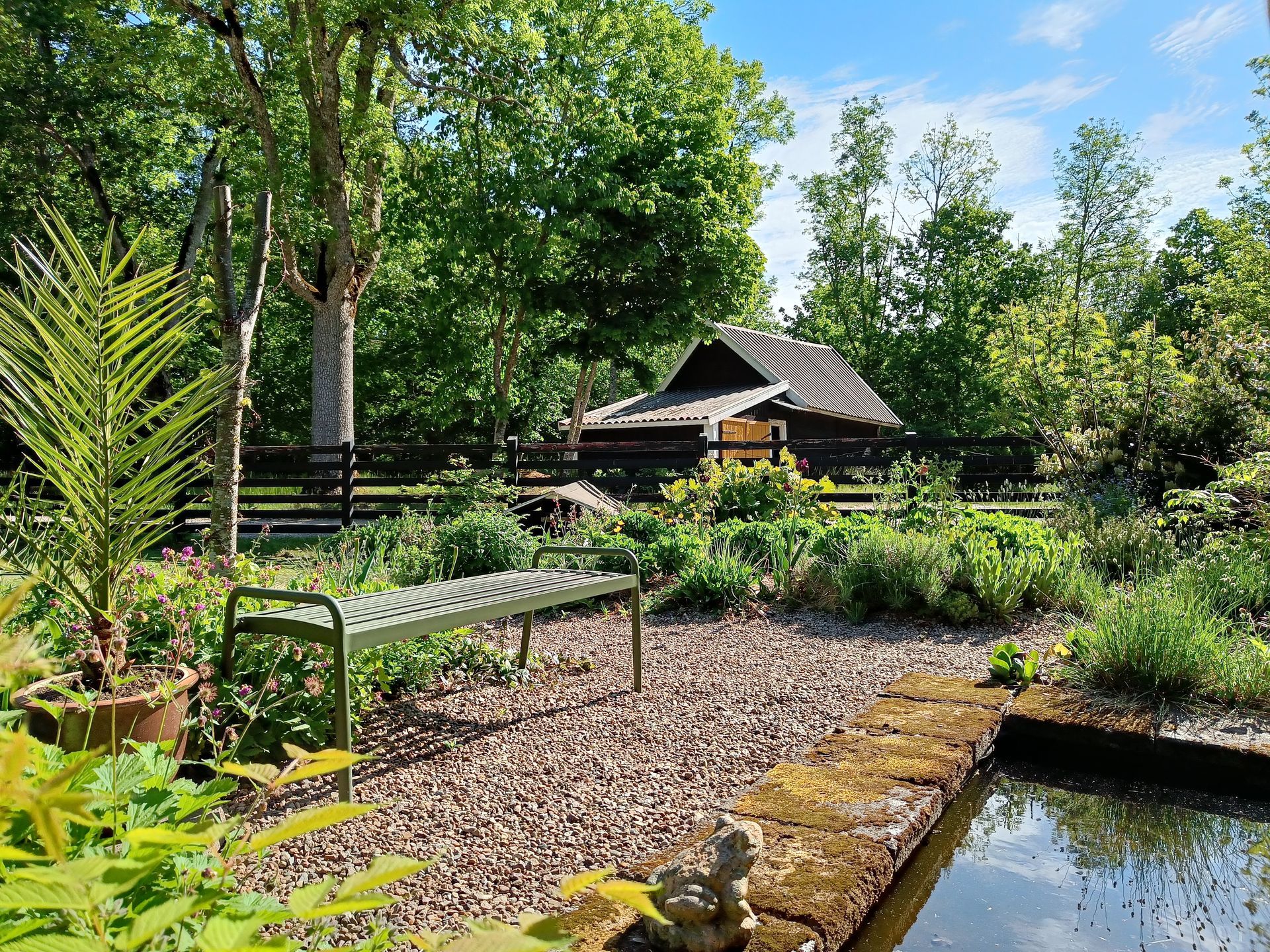 vy från Tom Lönneviks trädgård, med en liten damm i formell stil, en grusyta med en bänk och naturlika planteringar runtom