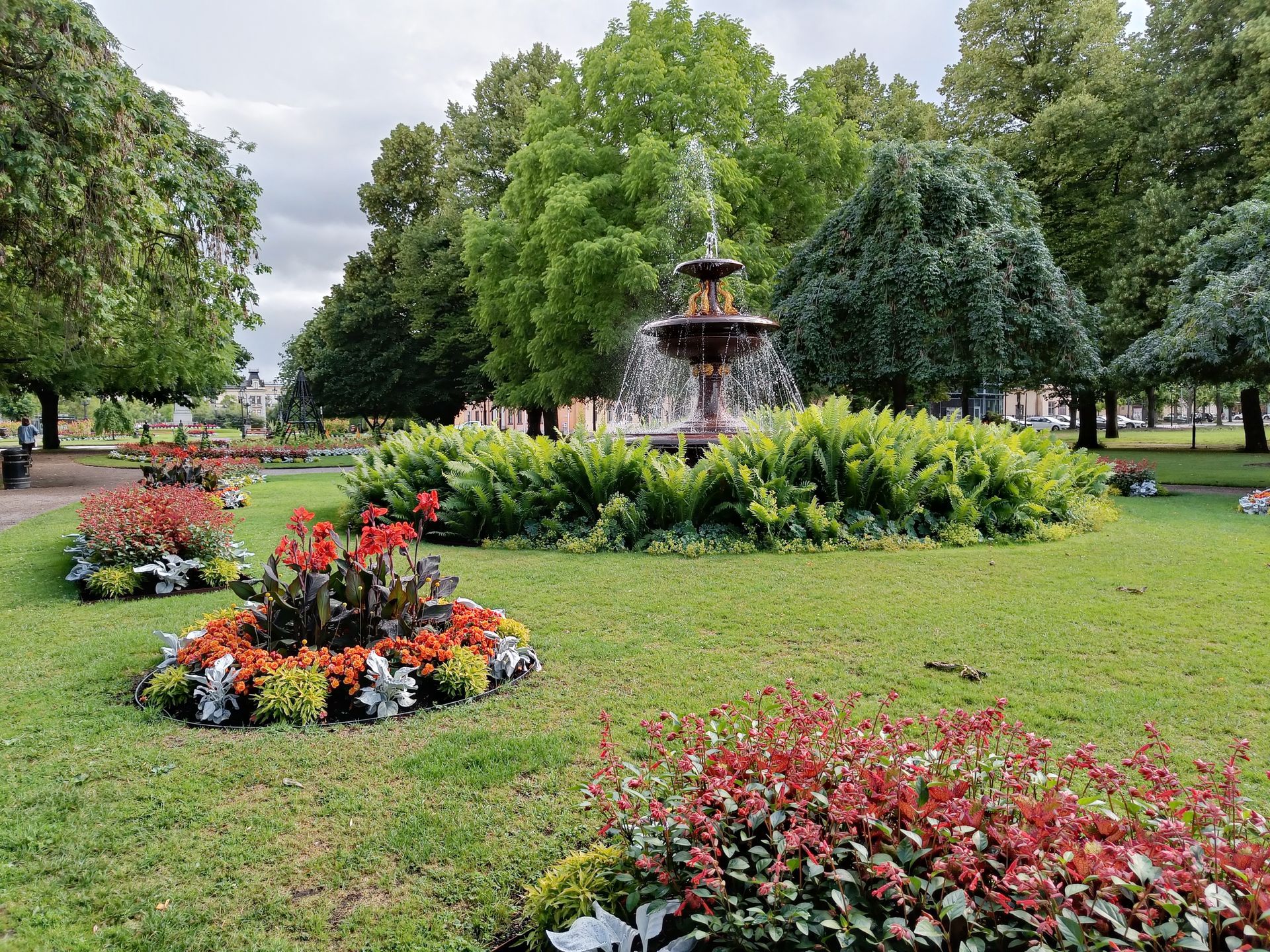 rundlar med sommarblommor och en pampig fontän med ormbunkar runt i Carl Johans park, Norrköping