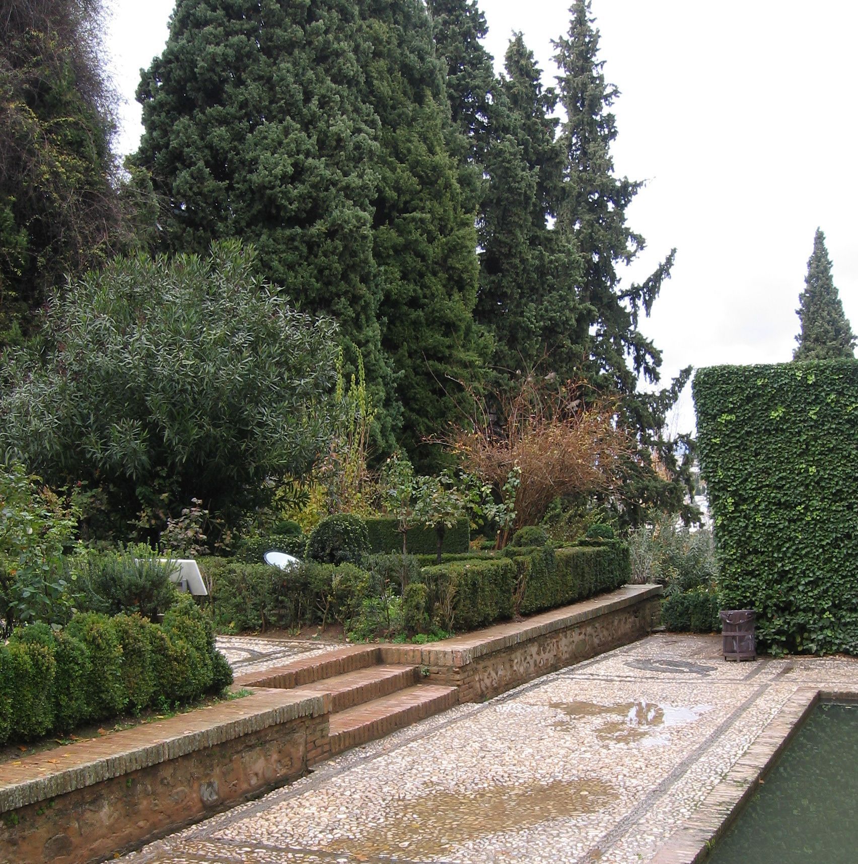 Trädgård i formell stil vid Alhambra, med många formklippa häckar och stenlagda strukturer med raka linjer.