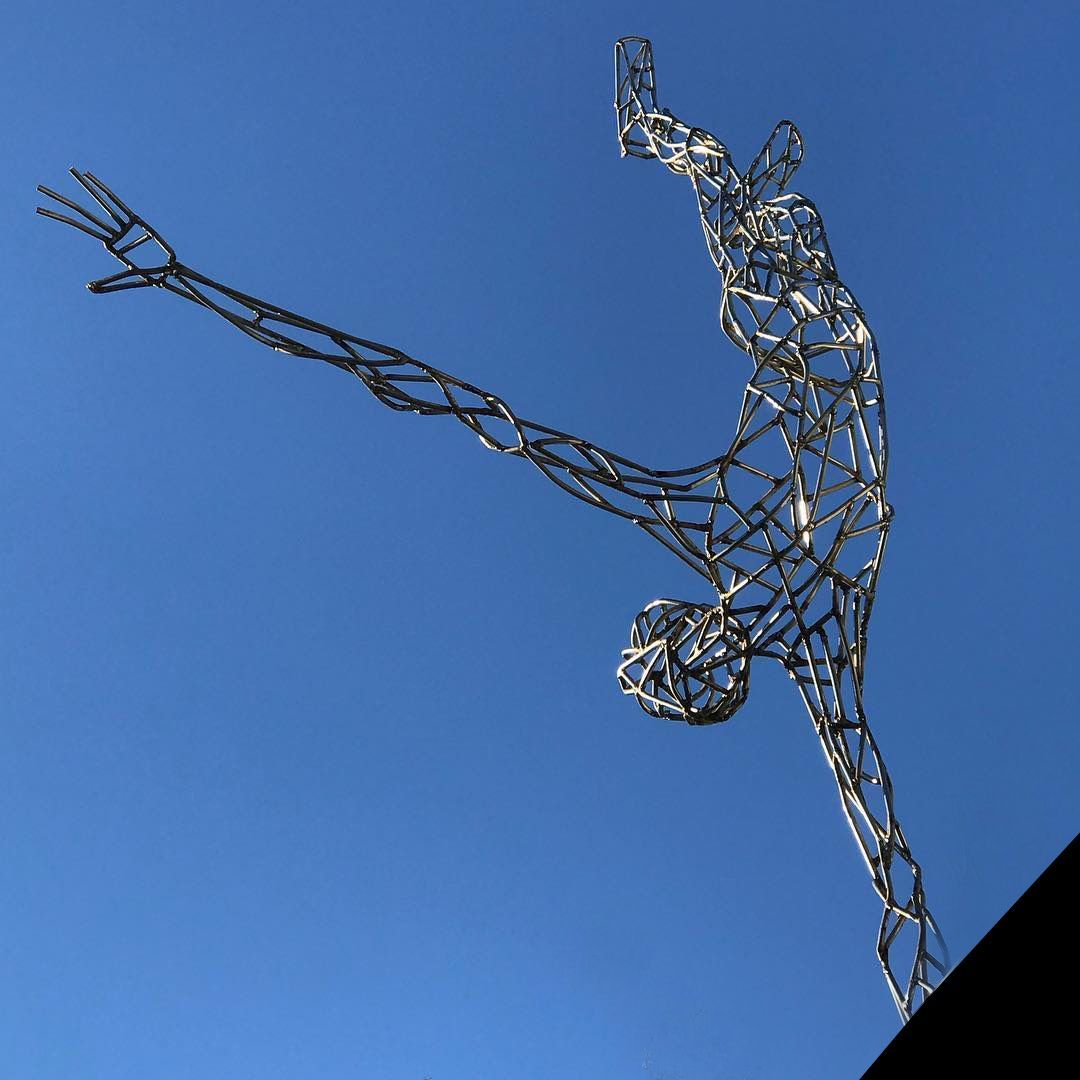 skulptur i metall i form av en person som står på en hand uppe vid taknocken på ett hyreshus