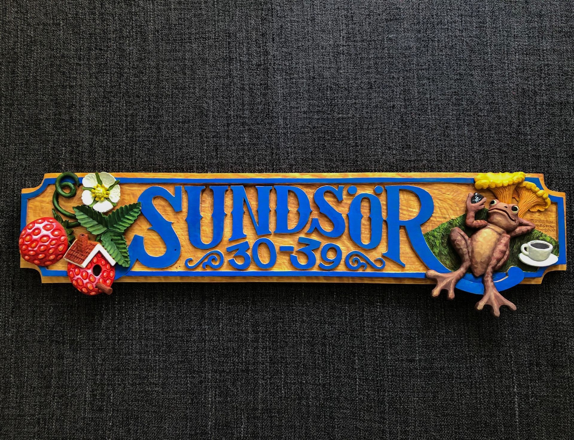 konstnärligt utformad skylt i trä av Jörgen Westin, med texten 'Sundsör'