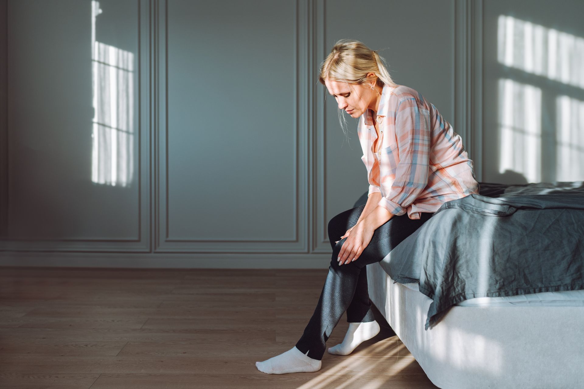 Person seated on bed gently massaging leg to ease varicose vein pain. Person seated on bed gently massaging leg to ease varicose vein pain.