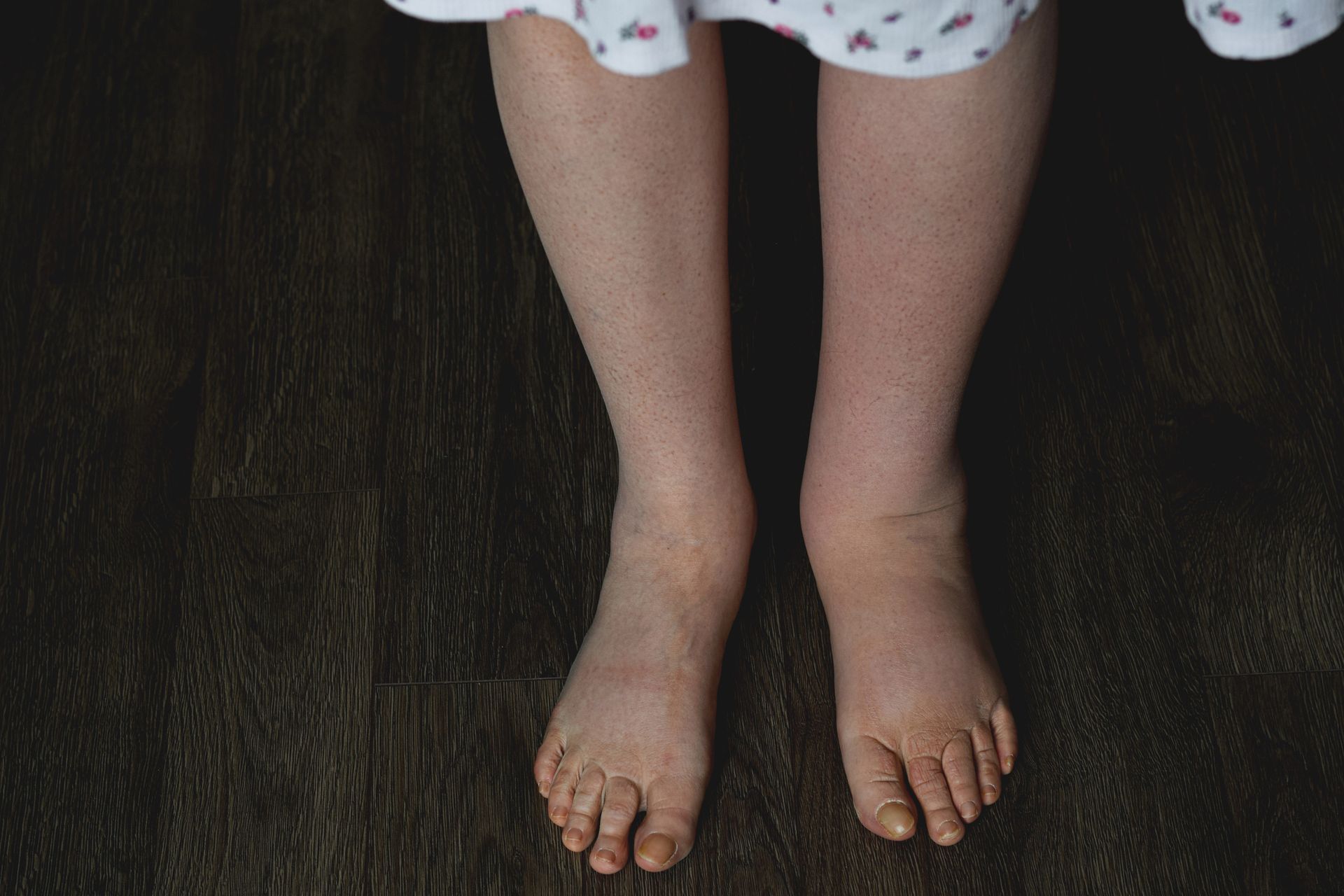 A child 's bare feet are standing on a wooden floor.