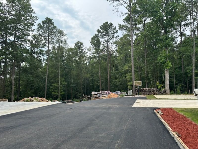 Asphalt road leading to wooded area with construction materials.