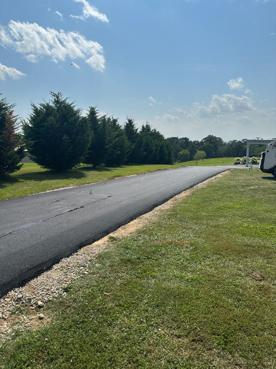 Newly paved black asphalt driveway next to a grassy area under a blue sky.