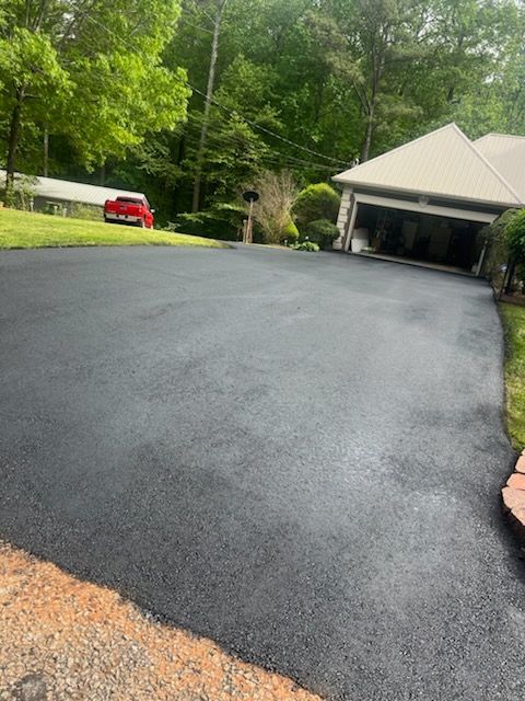 Newly paved black asphalt driveway leading to a house with a garage, red car in the distance.