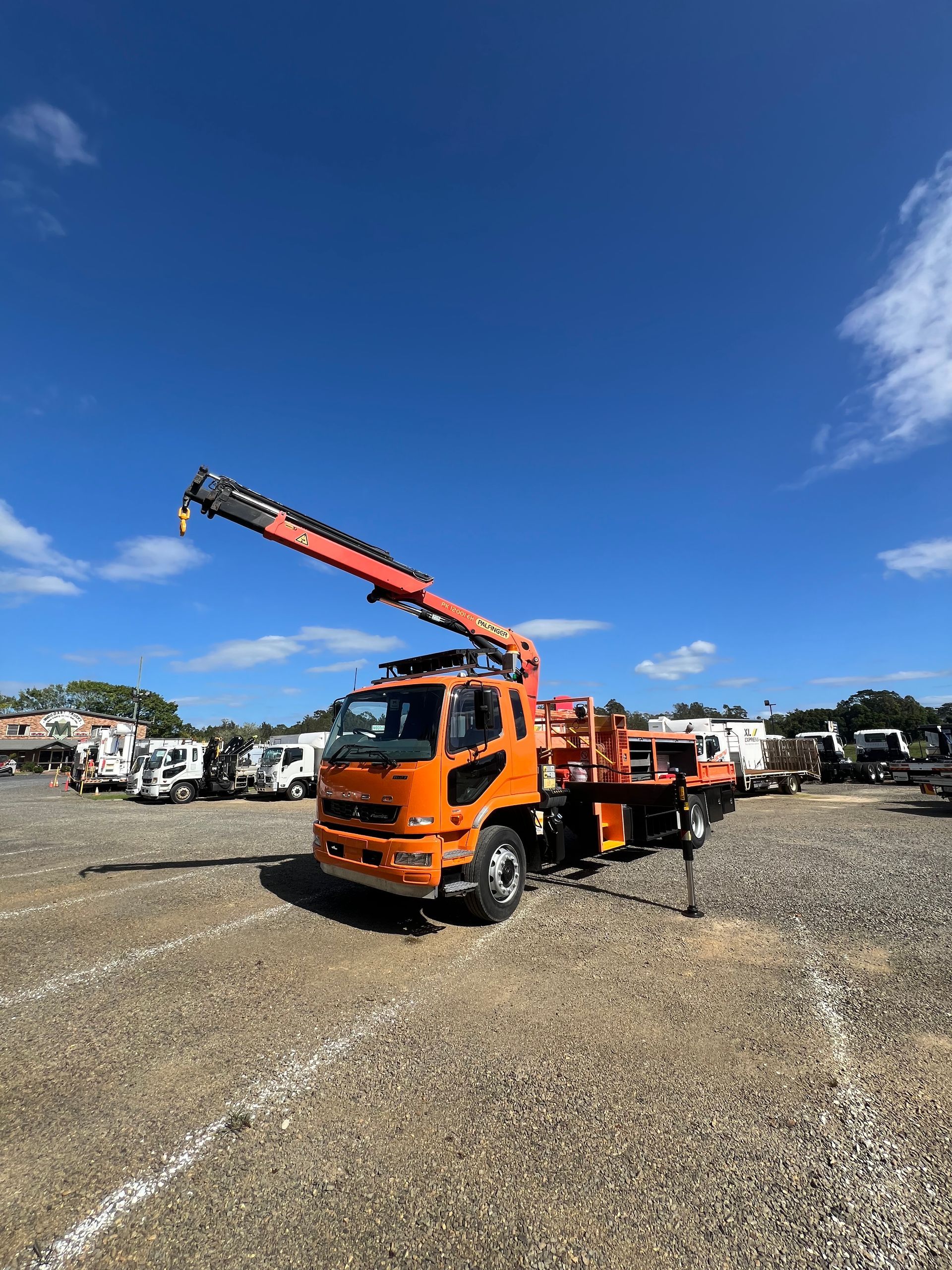 Orange crane truck parked on a gravel lot under a blue sky, boom extended. — North Coast Heavy Diesel In Thrumster, NSW