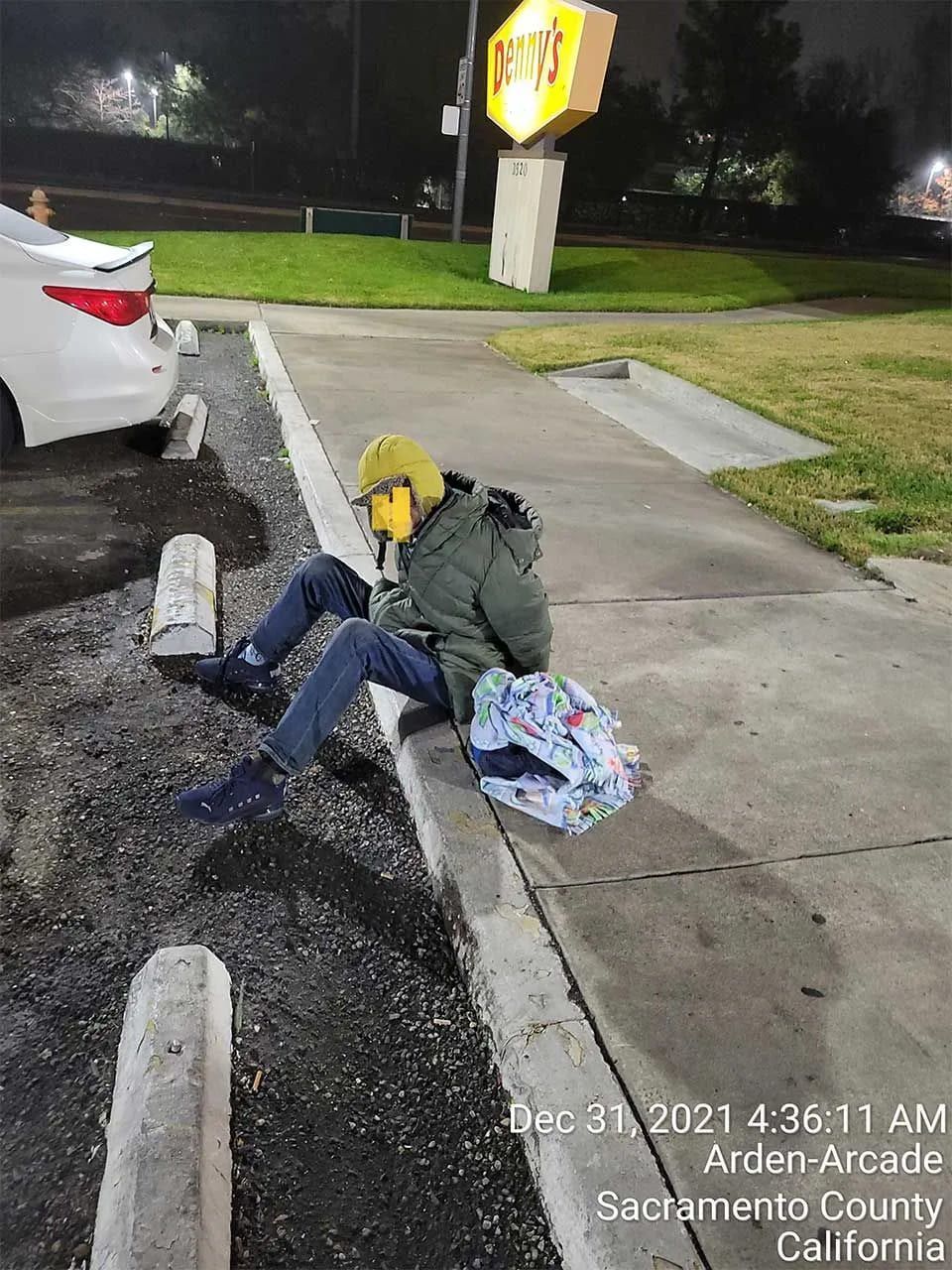 A person is sitting on the sidewalk in a parking lot.