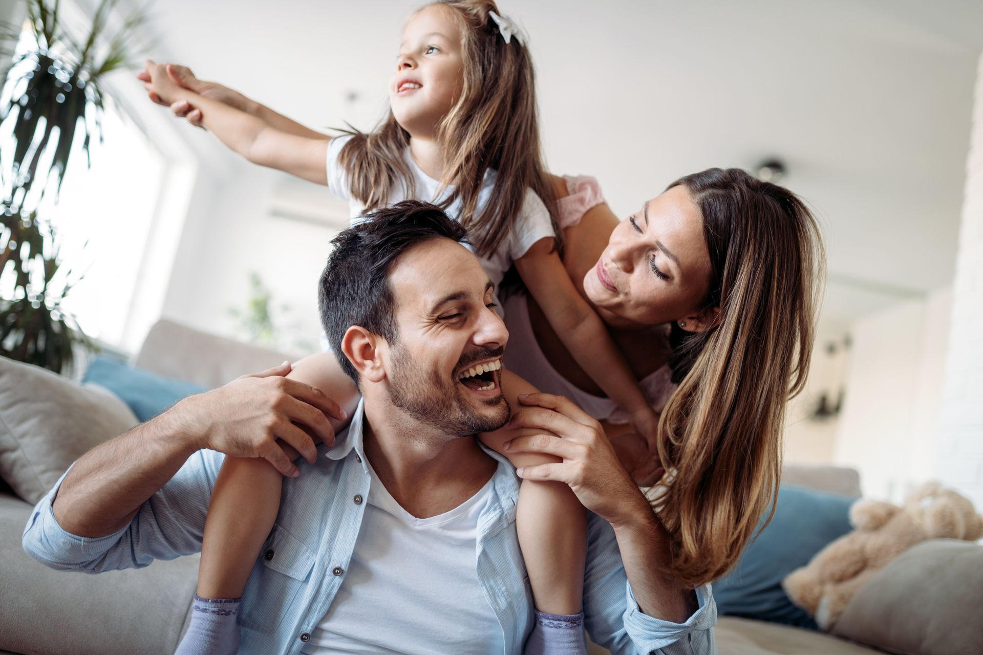 A man is carrying a little girl on his shoulders in a living room.