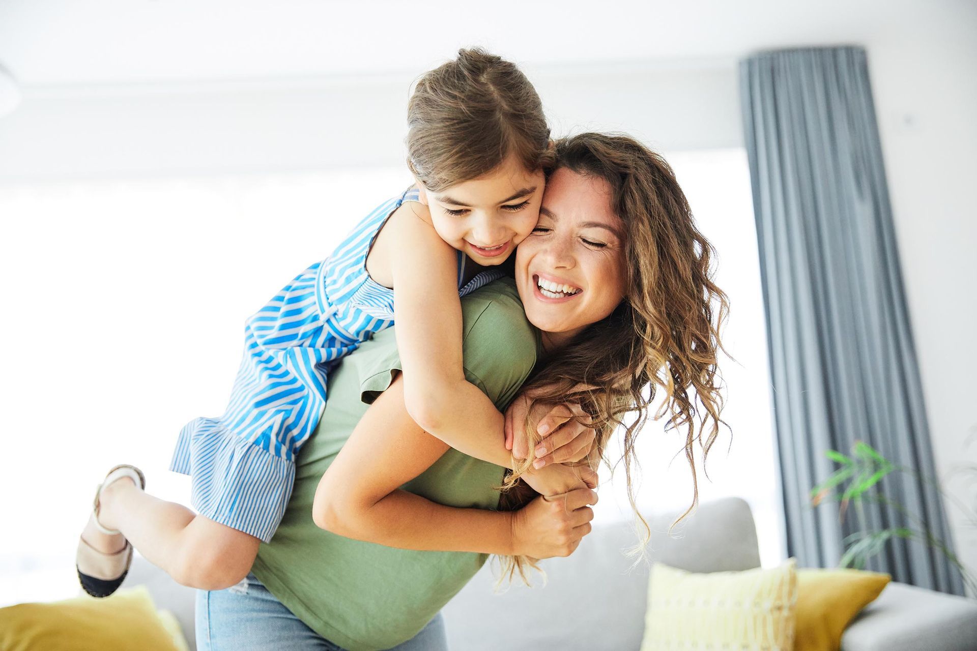 A woman is carrying a little girl on her back in a living room.