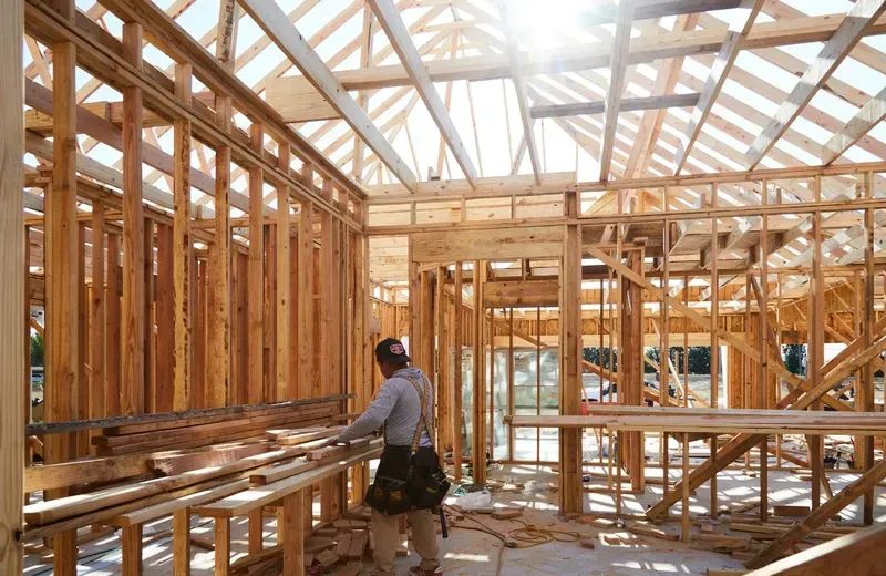 A man is standing in the middle of a wooden house under construction.