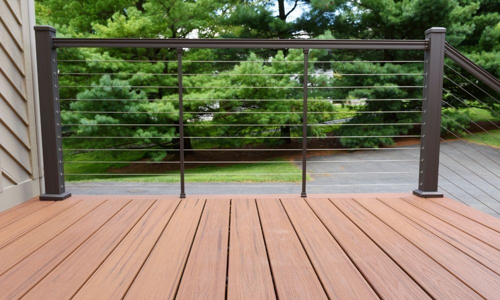 A wooden deck with a metal railing and trees in the background