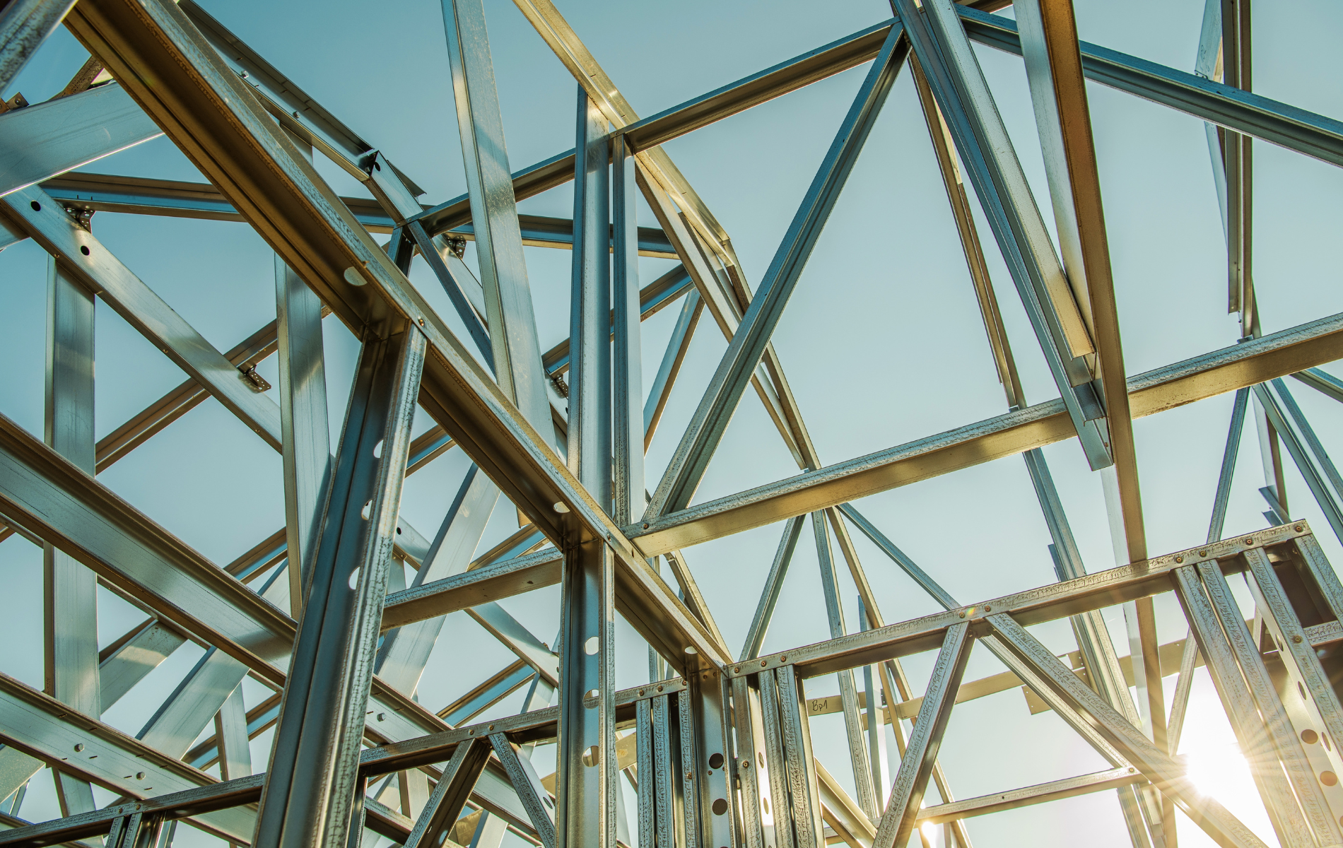 The sun is shining through the metal frames of a building under construction.