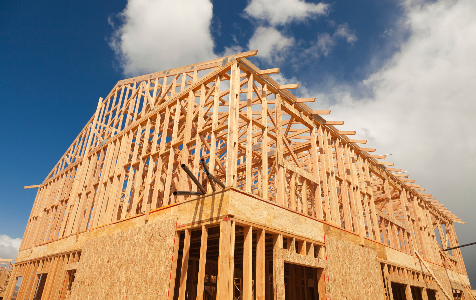 A wooden house is being built with a blue sky in the background.