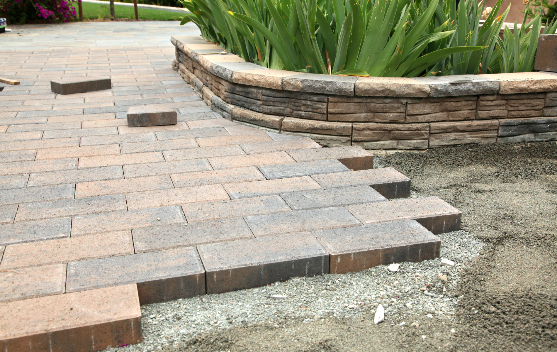 A brick walkway is being built next to a stone wall.