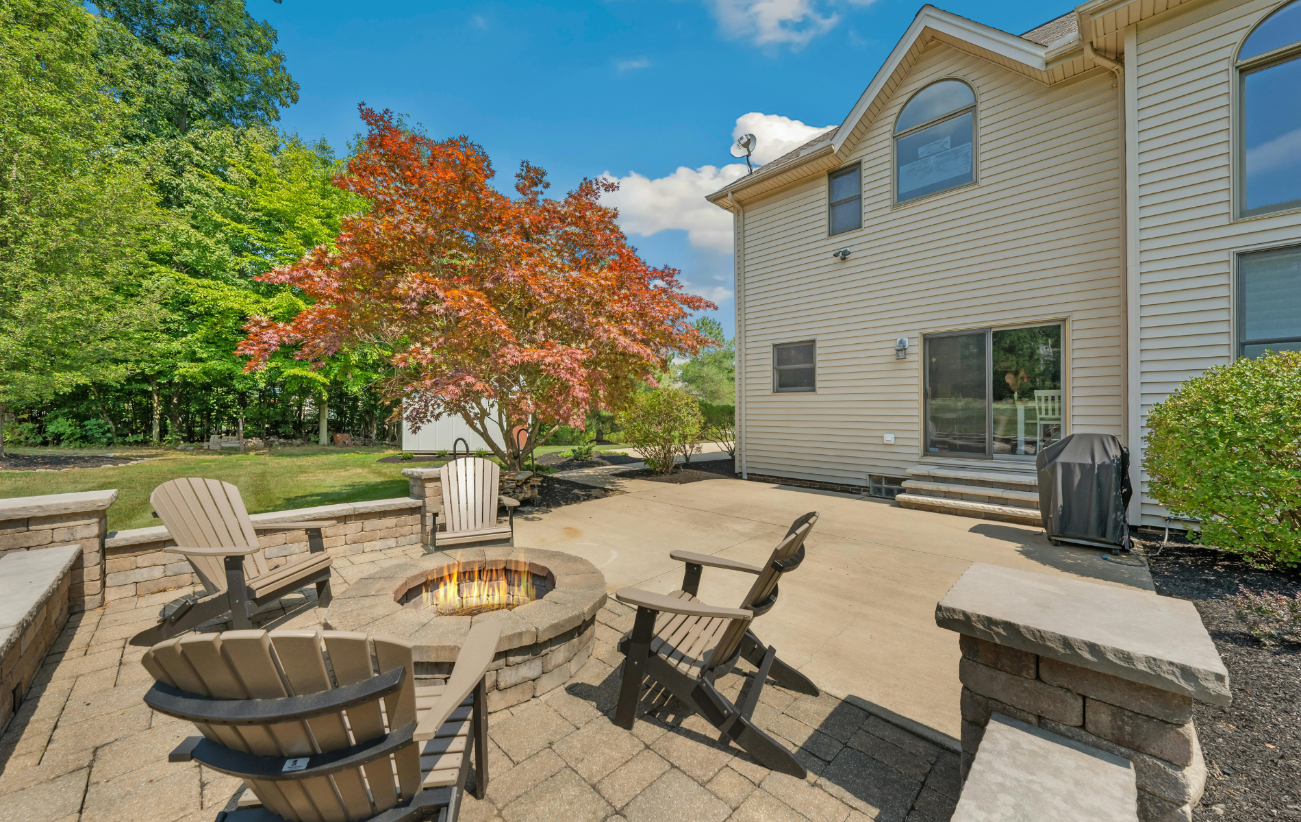 A patio with a fire pit and chairs in front of a house.