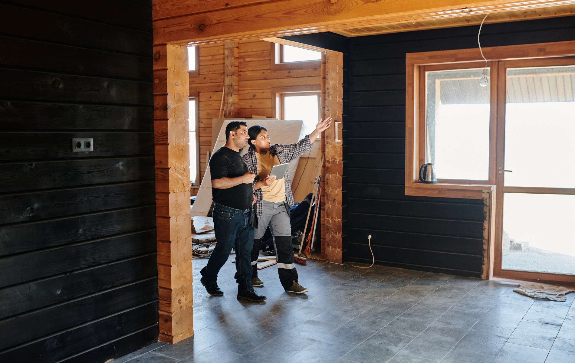 Two men are walking through an empty room in a wooden house.
