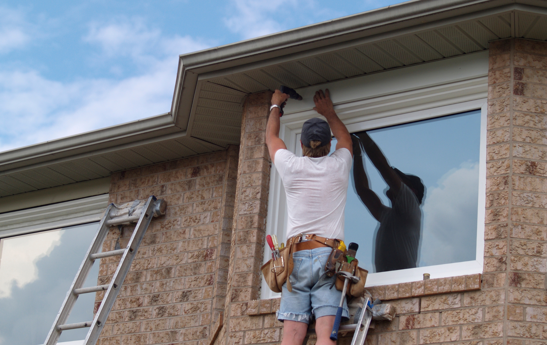 A man is standing on a ladder fixing a window