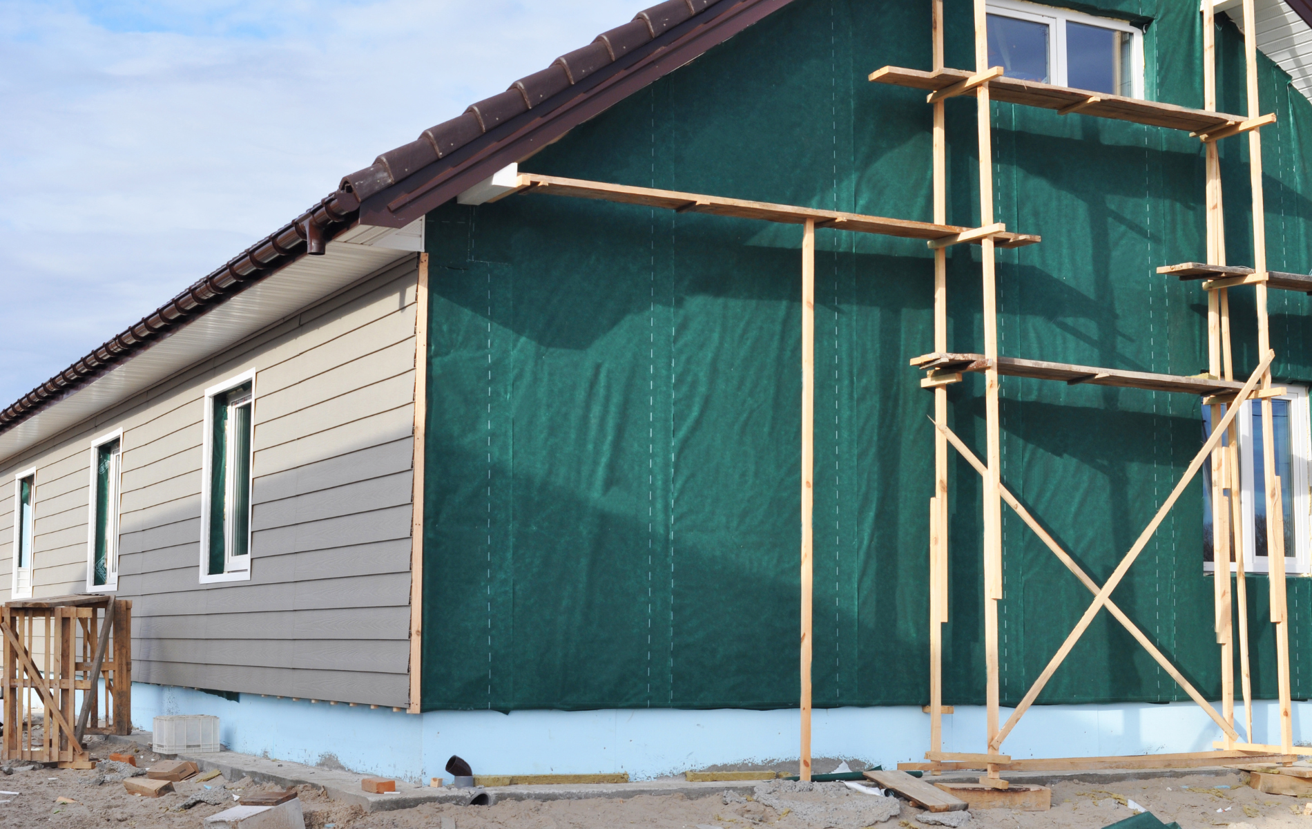 A house is being built with green siding and scaffolding