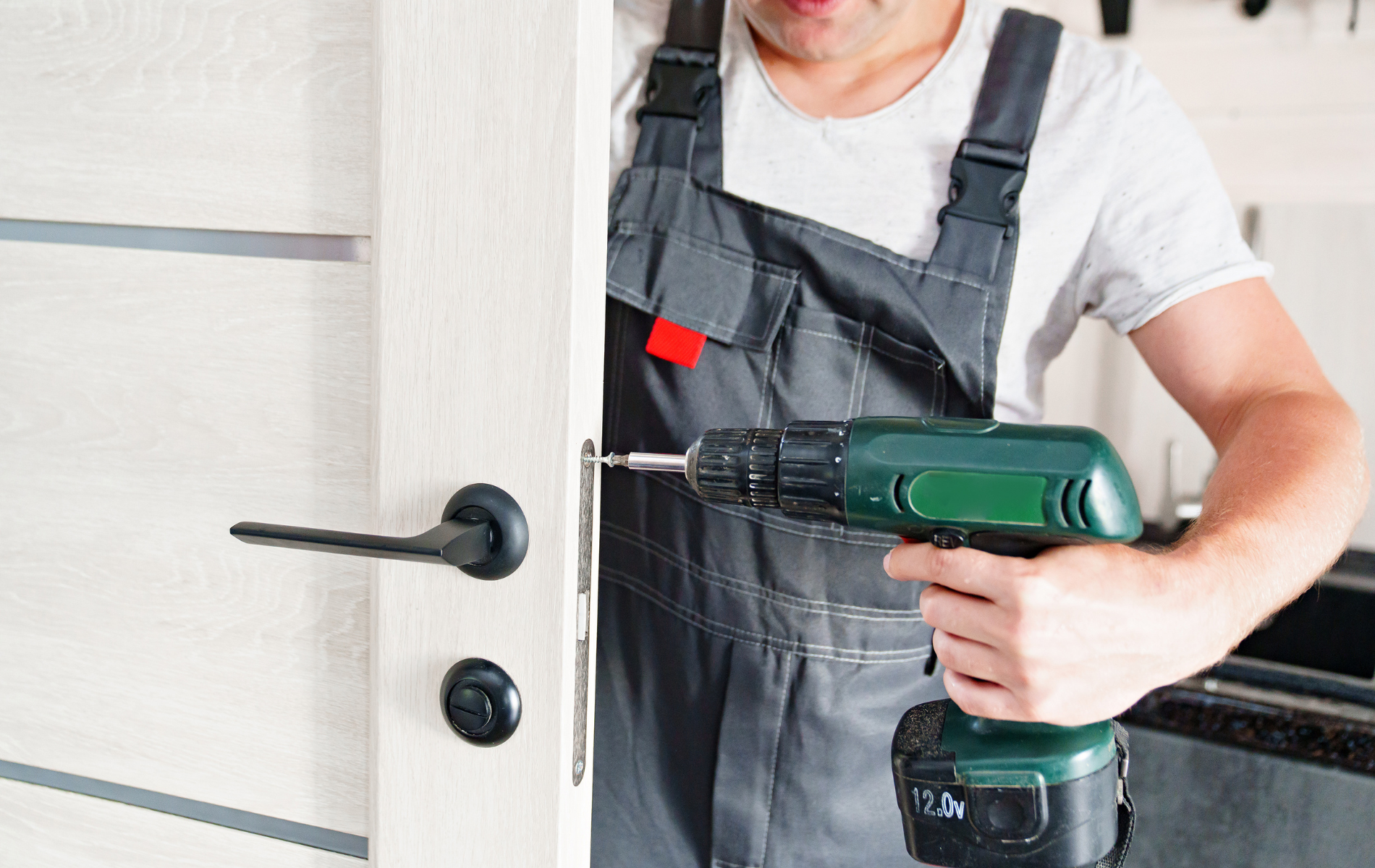 A man is using a drill to fix a door.